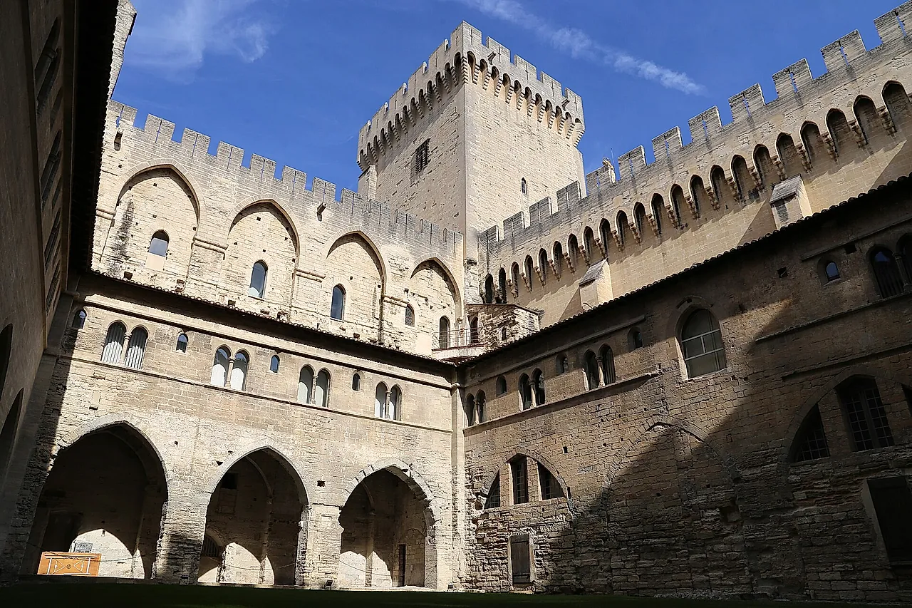El patio del claustro de Benedicto XII en el Palacio de los Papas: arcadas apuntadas bajo muros almenados y una torre