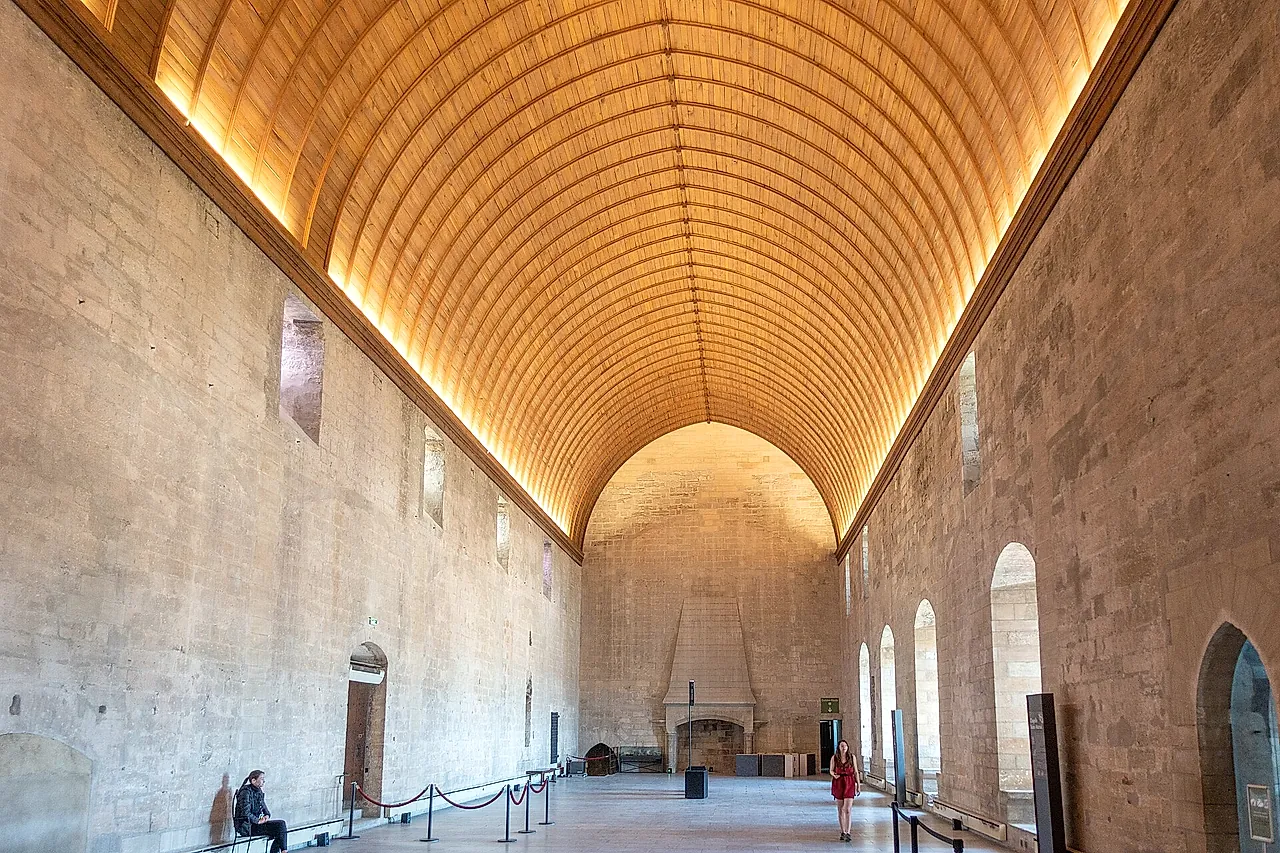 El Grand Tinel del Palacio de los Papas, una larga sala bajo una bóveda de cañón de madera iluminada, con una chimenea al fondo