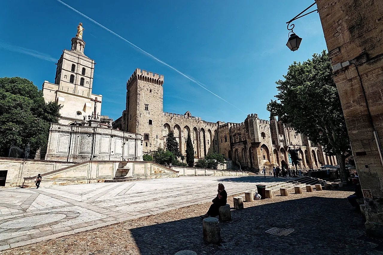 A Place du Palais com o campanário da catedral e sua Virgem dourada ao lado dos muros do palácio, sob sol forte